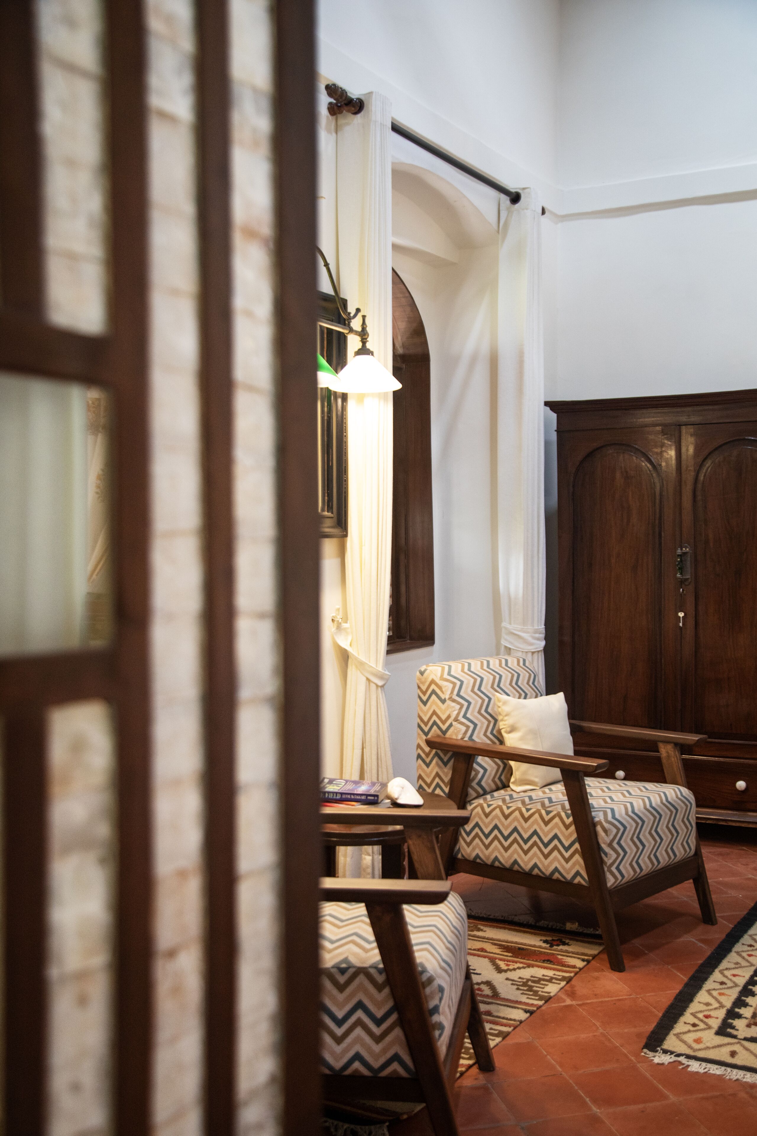 Una habitación con un armario de madera, dos sillones estampados, una lámpara de pie y una alfombra decorada.