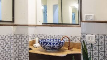 A bathroom with a blue and white ceramic sink, a wooden countertop, a mirror above the sink, and a potted plant.