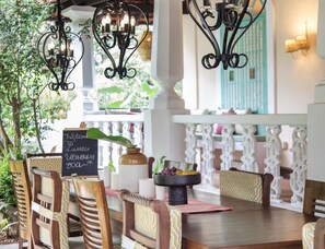 Un área de comedor al aire libre con sillas y mesas de madera, candelabros metálicos decorativos y un letrero de pizarra.