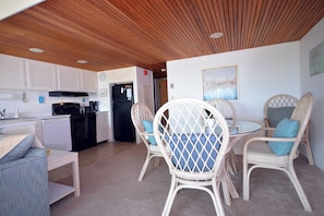 A kitchen with white cabinets, a black refrigerator, and a dining area with wicker chairs and a table.