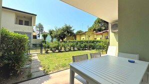 Un patio con mesa y sillas, rodeado de un jardín y un edificio de fachada amarilla.