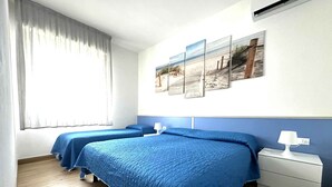 Habitación de hotel con dos camas, un ventanal con cortinas, un aire acondicionado instalado en la pared y una mesita de noche con lámpara.