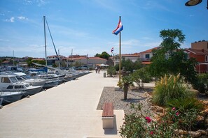 Un port de plaisance avec des bateaux amarrés, un mât portant un drapeau et un sentier bordé de bancs et de plantes.