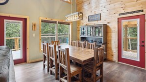 A wooden interior with a dining table and chairs, a kitchen area, and large windows. - Brand New 5 Bedroom with Arcade, WiFi, Hot Tub!  Located in Thunder Mtn Resort! (Sevierville)