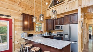 A spacious kitchen with granite countertops, stainless steel appliances, and wooden bar stools. - Brand New 5 Bedroom with Arcade, WiFi, Hot Tub!  Located in Thunder Mtn Resort! (Sevierville)