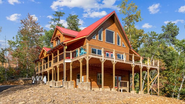 A large wooden cabin with a red roof, multiple balconies, and a stone foundation. - Brand New 5 Bedroom with Arcade, WiFi, Hot Tub!  Located in Thunder Mtn Resort! (Sevierville)