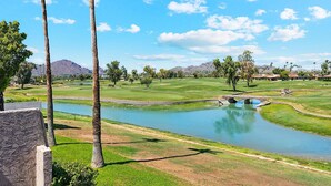 A golf course with a pond, palm trees, and a mountain in the background.