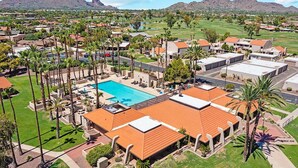 A resort with a swimming pool, palm trees, and a mountainous backdrop.