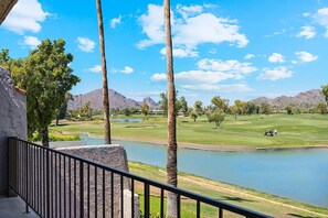 Un campo de golf con un estanque, palmeras y montañas al fondo.