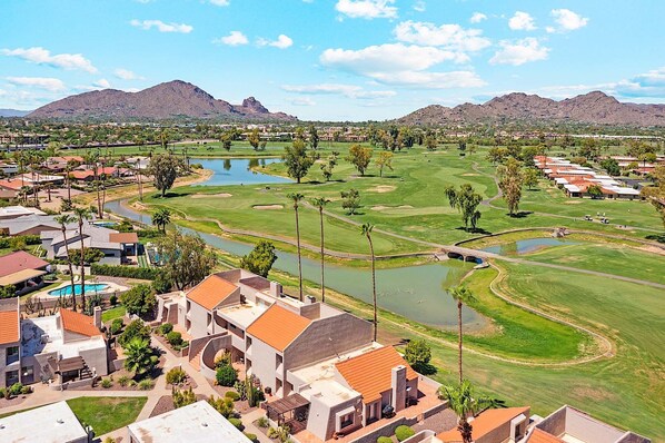 Un campo de golf con un puente, un estanque y edificios residenciales con tejados de tejas rojas.