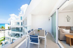 A balcony with a dining table, chairs, and a view of the ocean.