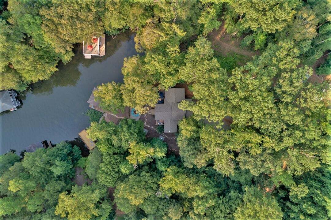Une vue aérienne d’une maison entourée d’une forêt dense et d’un petit quai.