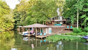 Een vakantiehuis aan het meer met een steiger, een overdekte veranda en een terras.