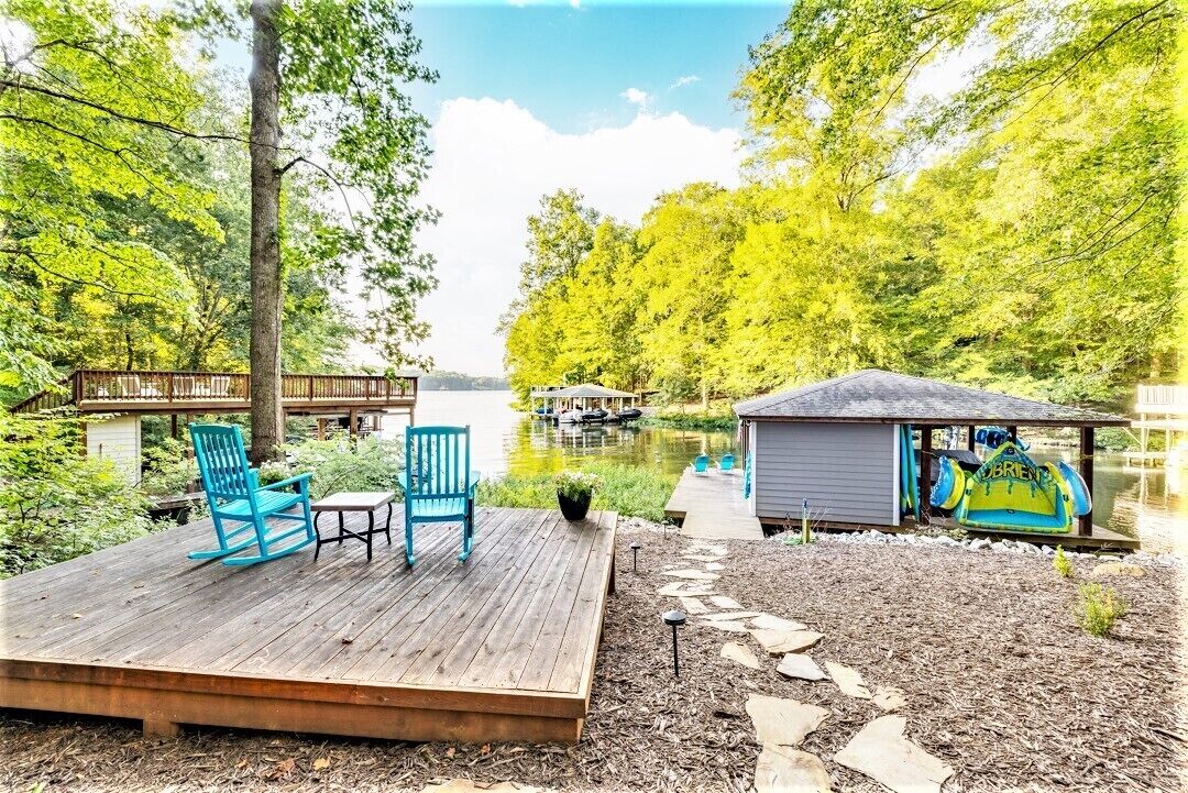 A wooden deck with chairs and a small shed by a lake.