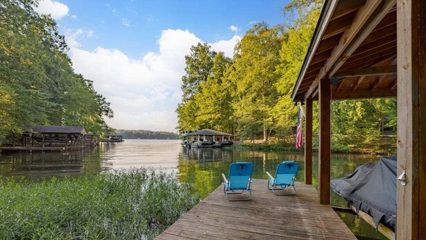 Een houten steiger met twee blauwe stoelen en een overdekte zithoek met uitzicht op een meer.
