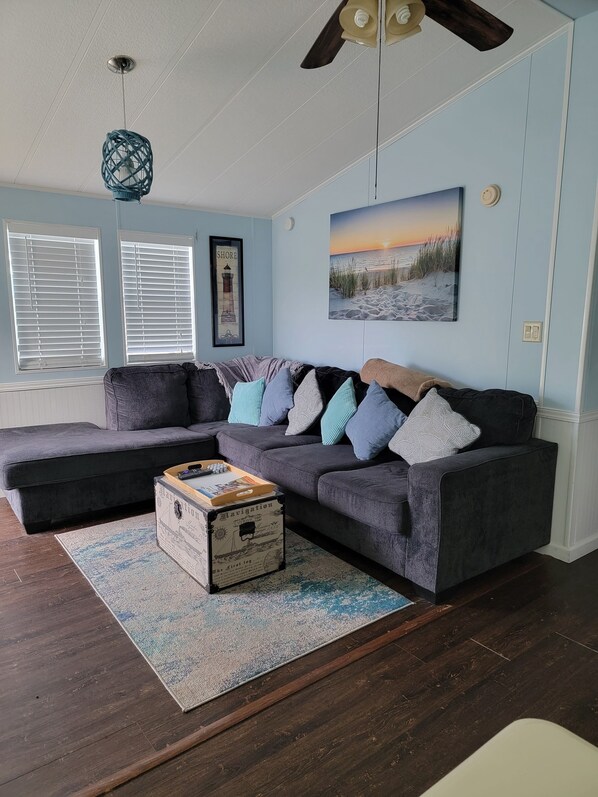 A living room with a sectional sofa, a decorative box, a rug, and a painting of a beach scene. - Home in private gated community - Assateague Pointe/tons of fun amenities (Berlin)