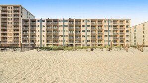 A beachfront hotel with multiple floors, balconies, and a sandy beach in front.