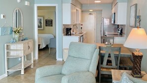 A living room with a sofa, armchair, and coffee table, a dining area with a table and chairs, and a kitchen in the background.