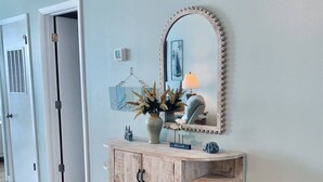 A wooden console with a mirror, a vase with dried flowers, and a lamp.