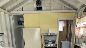 A compact kitchen with a stove, refrigerator, and a small sink. There is a yellow chair at a round table in the center.