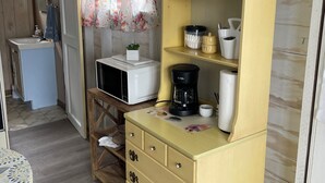 A cozy kitchen with wooden cabinets, a microwave, a coffee maker, and a shelf with cups and a salt shaker.