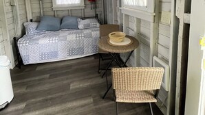 Una cabaña pequeña y rústica con una cama, una mesa de comedor y un ventilador de techo.