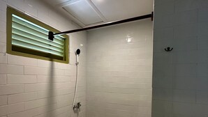 A small, tiled bathroom with a toilet, a shower, and a window with blinds. - Honu Studio Living Bali (Pererenan)