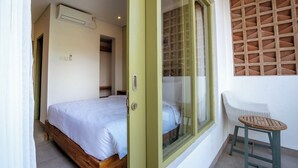 A bedroom with a bed, a window with a grid pattern, a chair, and a small table. - Honu Studio Living Bali (Pererenan)