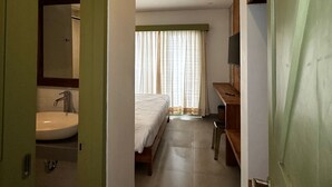 A narrow hallway leading to a bedroom with a bed, a desk, and a window with curtains. - Honu Studio Living Bali (Pererenan)