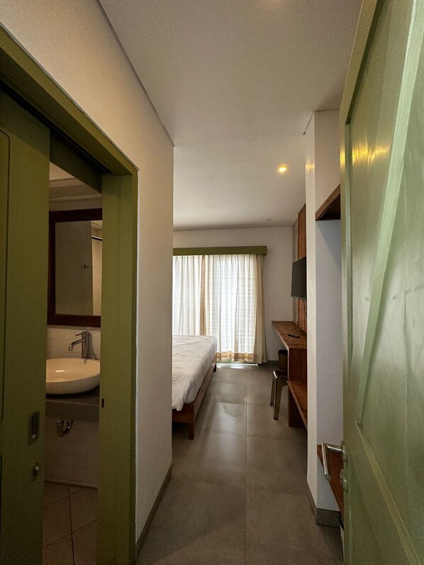 A narrow hallway leading to a bedroom with a bed, a desk, and a window with curtains. - Honu Studio Living Bali (Pererenan)