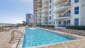 A swimming pool with a brick deck, surrounded by a white building with balconies. - 705 St Maarten - Daytona Beach Oceanfront Vacations, Inc (Daytona Beach Shores)