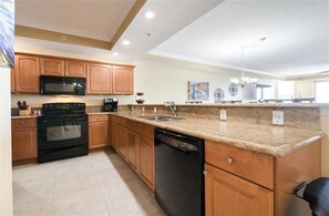 A kitchen with wooden cabinets, a black stove, a dishwasher, granite countertops, and a microwave. - #705 St. Maarten 3/3 Luxury Oceanfront Condo Daytona Beach Shores (Daytona Beach Shores)