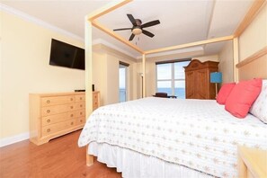 Une chambre à coucher avec un lit à baldaquin, une commode en bois, un ventilateur de plafond et un téléviseur fixé au mur.