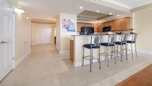 A spacious kitchen with wooden cabinets, a central island with bar stools, and a microwave. - 705 St Maarten - Daytona Beach Oceanfront Vacations, Inc (Daytona Beach Shores)