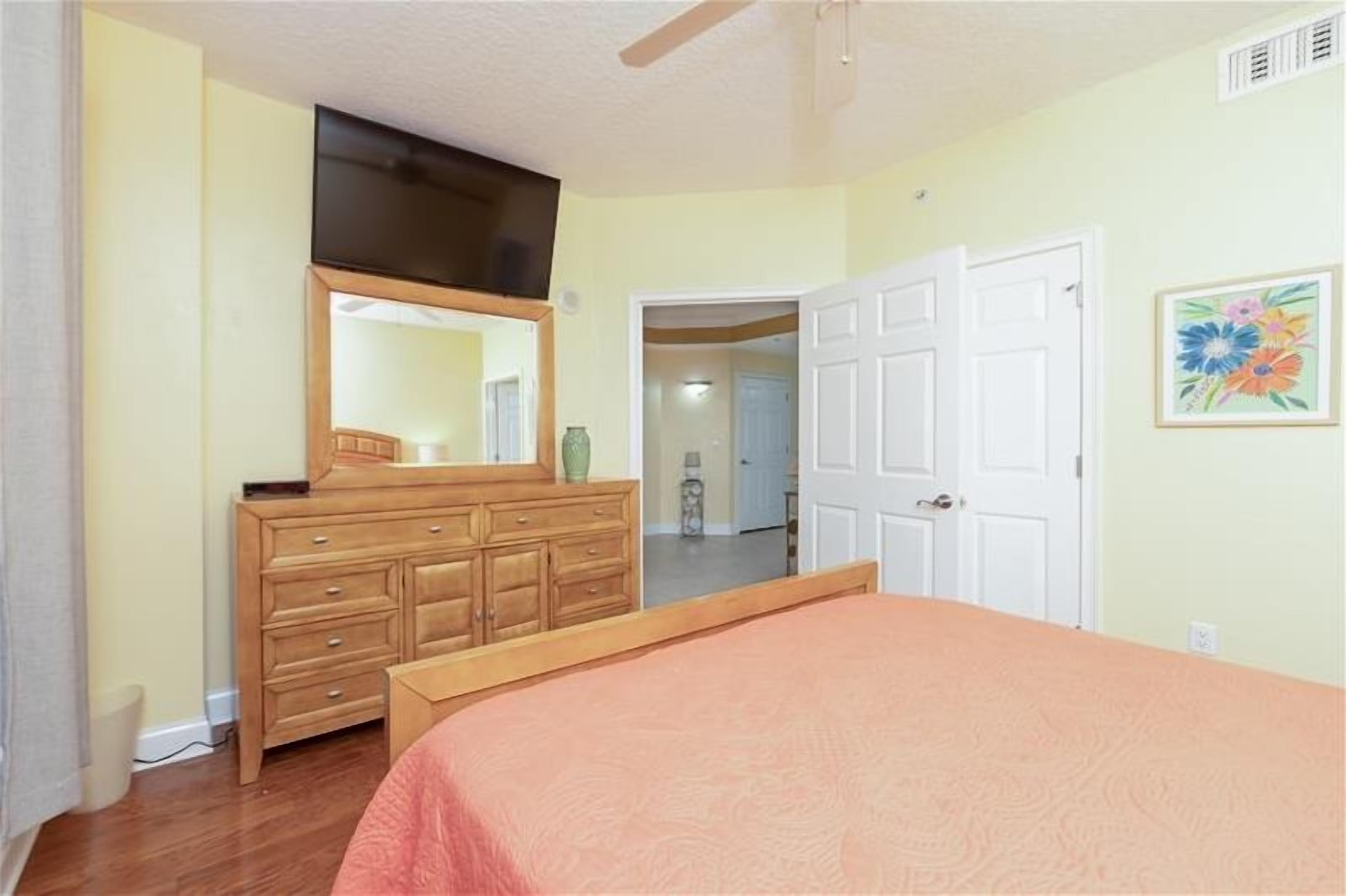 A bedroom with a bed, dresser, mirror, and a door leading to another room.