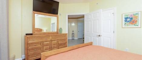 Un dormitorio con cama, cómoda, espejo y una puerta que da a otra habitación.