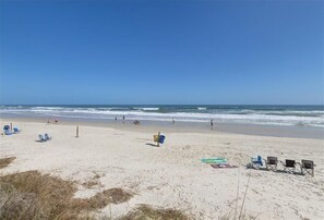 Une plage avec un ciel dégagé, des vagues et des chaises de plage.