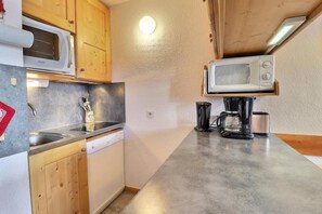 A compact kitchen with wooden cabinets, a built-in microwave, a coffee maker, and a dishwasher.