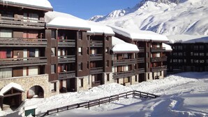 Ett hotell med flera våningar, balkonger, en grundmur av sten och snötäckta tak, som ligger inbäddat i ett bergigt landskap.