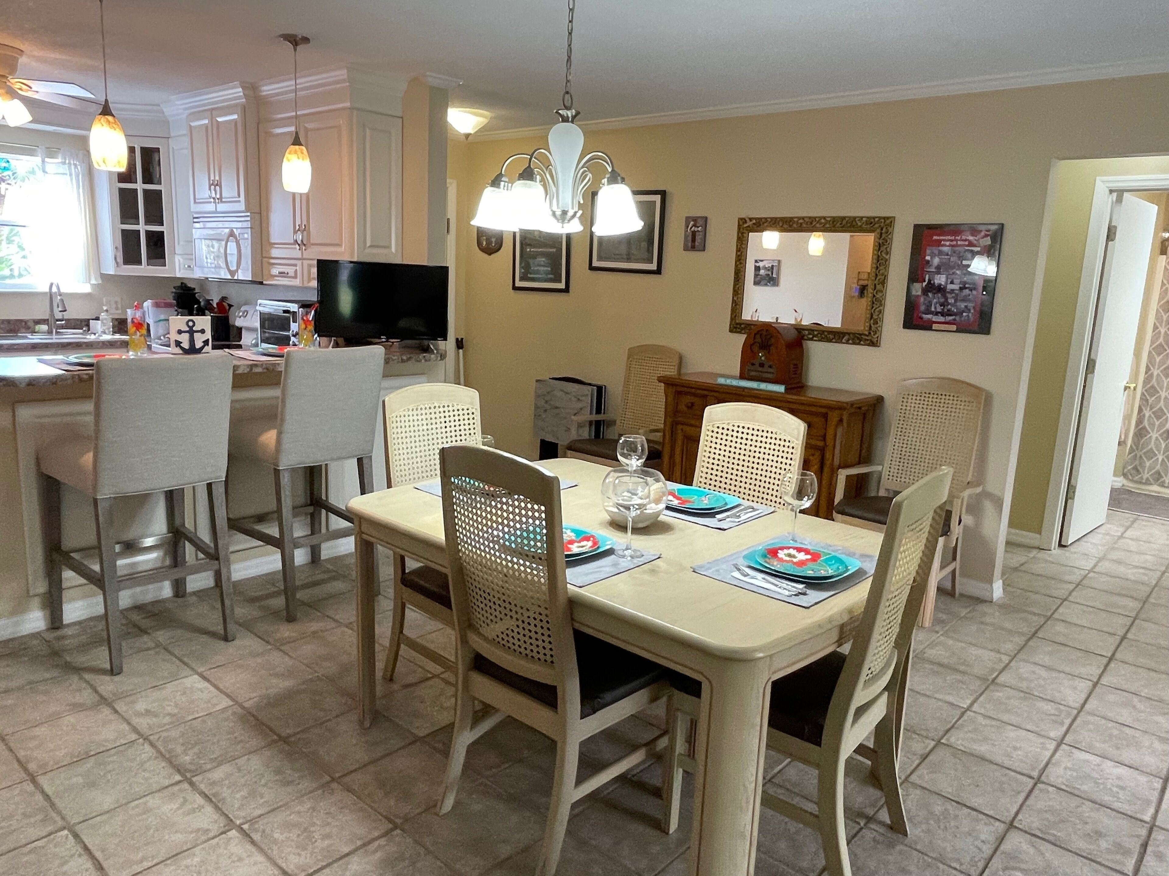 A dining area with a table set for four, surrounded by chairs. A television is mounted on the wall above the table.