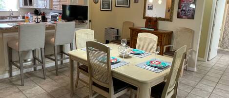 A dining area with a table set for four, surrounded by chairs. A television is mounted on the wall above the table.