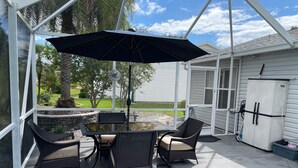 An outdoor patio with a table and chairs, a clock, and a view of a house and trees. - Welcome to Your Ideal Getaway in The Villages! (The Villages)