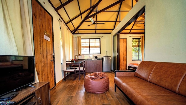Una sala de estar acogedora con piso de madera, un sofá de cuero marrón, un televisor y un comedor con una mesa y sillas.