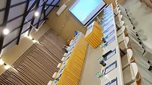 Una larga mesa de conferencias con sillas, una pantalla de proyector y un techo con tragaluces.
