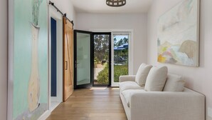 A modern interior with a wooden floor, a white sofa, and a glass door leading to an outdoor area. - Spectacular Healdsburg Manor-4BR/4.5BA, POOL+2 SPA! (Healdsburg)
