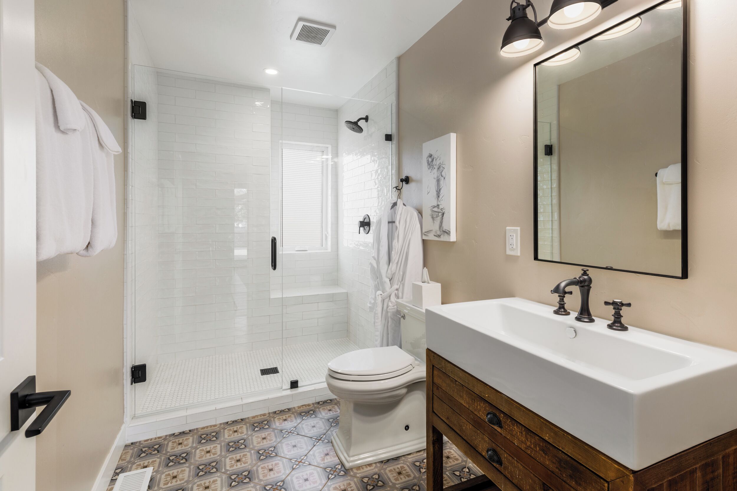 A modern bathroom with a glass-enclosed shower, a white toilet, a wooden vanity with a sink, and a large mirror.