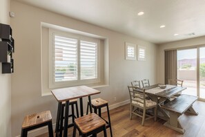 A dining area with a wooden table and chairs, a window with blinds, and a view of the outdoors.