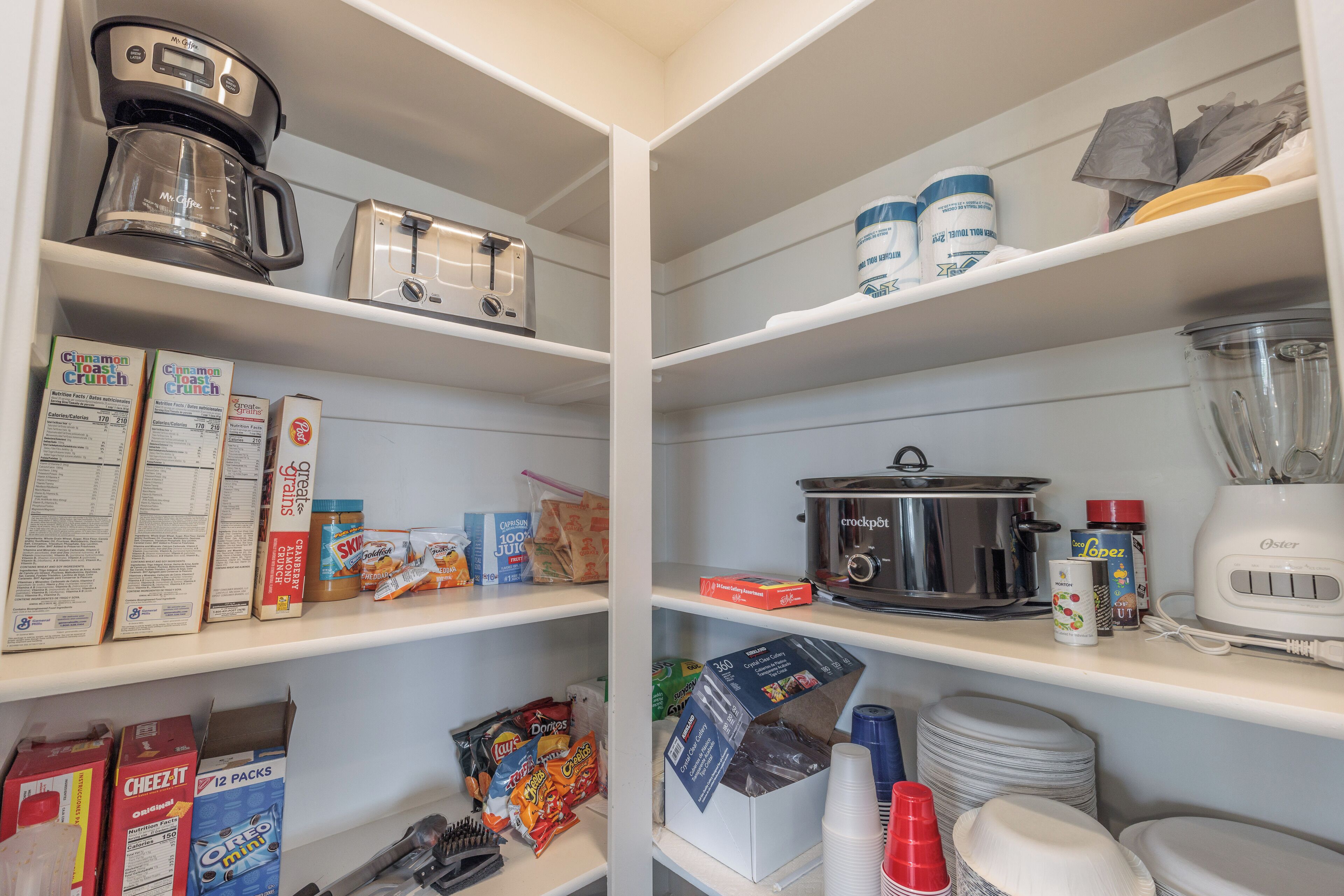 Een geordende voorraadkast met verschillende etenswaren, keukenapparatuur en opbergcontainers.