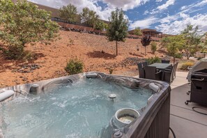 Relax in a serene outdoor setting with a hot tub surrounded by lush greenery and a paved walkway.