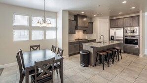 A modern kitchen with a dining area, featuring a central island with stools, dark cabinetry, and stainless steel appliances. - Family 4BR Sleeps 23 - Private Hot Tub Near Pool (St. George)